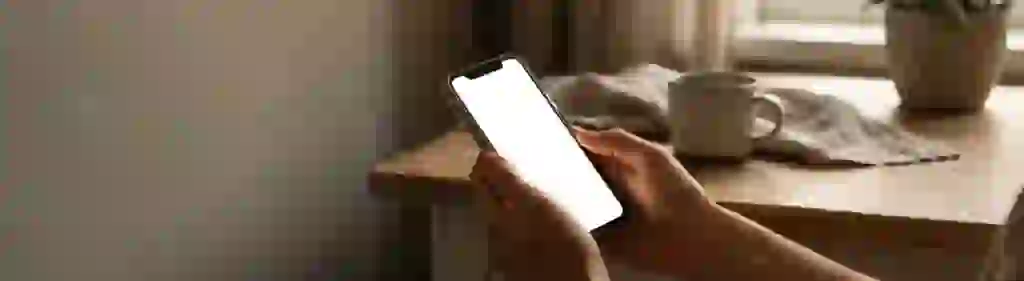 Руки держат телефон в сумеречной комнате у окна